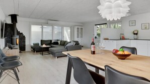 Ein zeitgemäßer Wohnraum mit Kamin aus Stein, einem Essbereich mit Holztisch und einem großen Fenster für natürliches Licht.