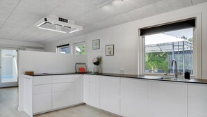 Eine moderne Küche mit weißen Schränken, einem eingebauten Ofen und einem großen Fenster mit Blick ins Freie.