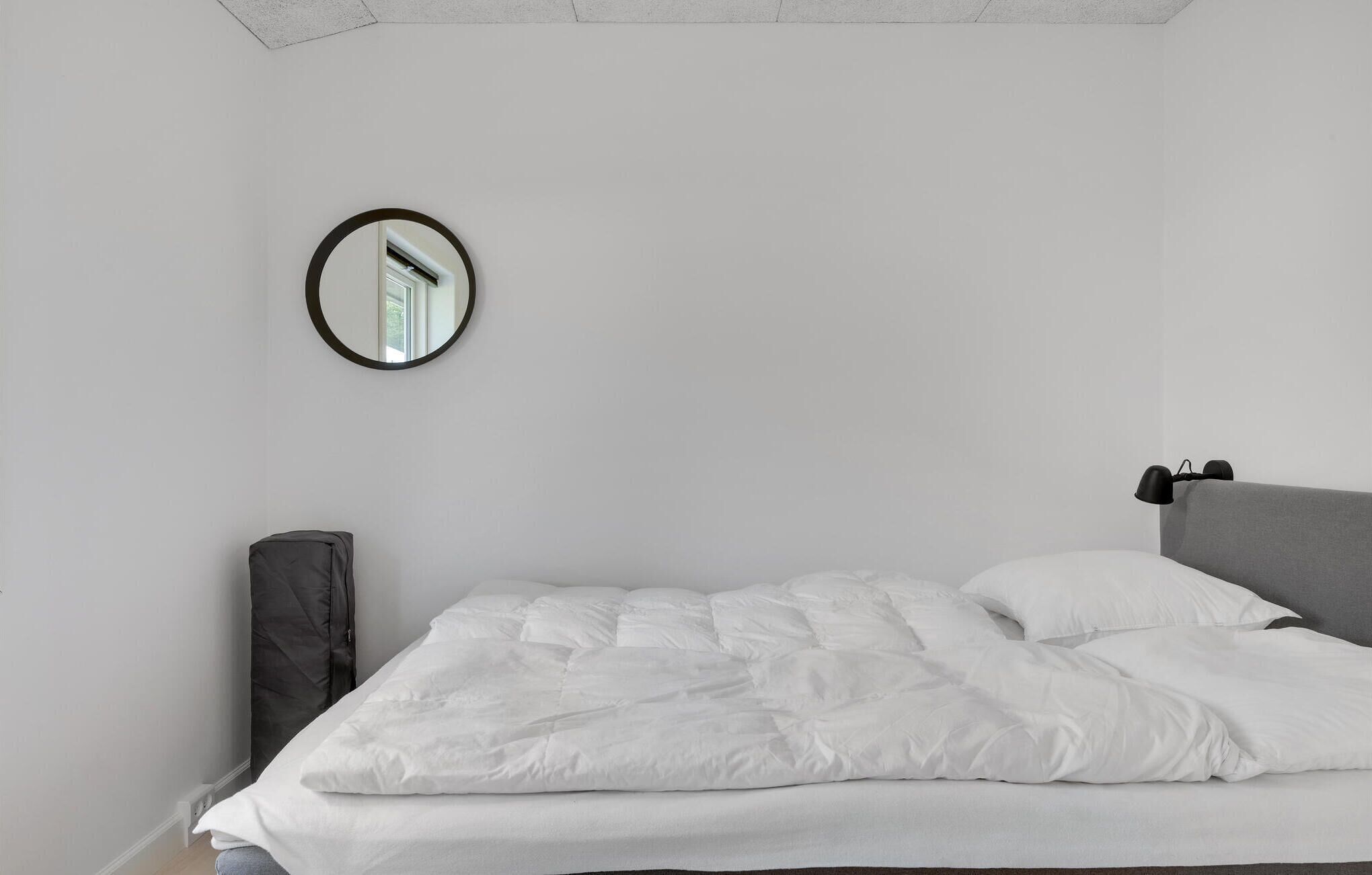 A minimalist bedroom with a single bed, a round mirror, and a gray headboard.