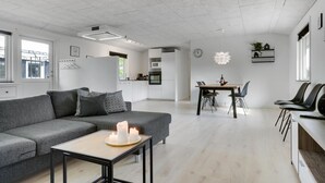 Ein modernes Wohnzimmer mit einem grauen Sofa, einem Couchtisch mit Kerzen und einem Essbereich mit einem Holztisch und Stühlen.