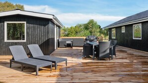 Eine Holzterrasse mit Liegestühlen und einem Tisch, umgeben von dunklen Holzhütten.