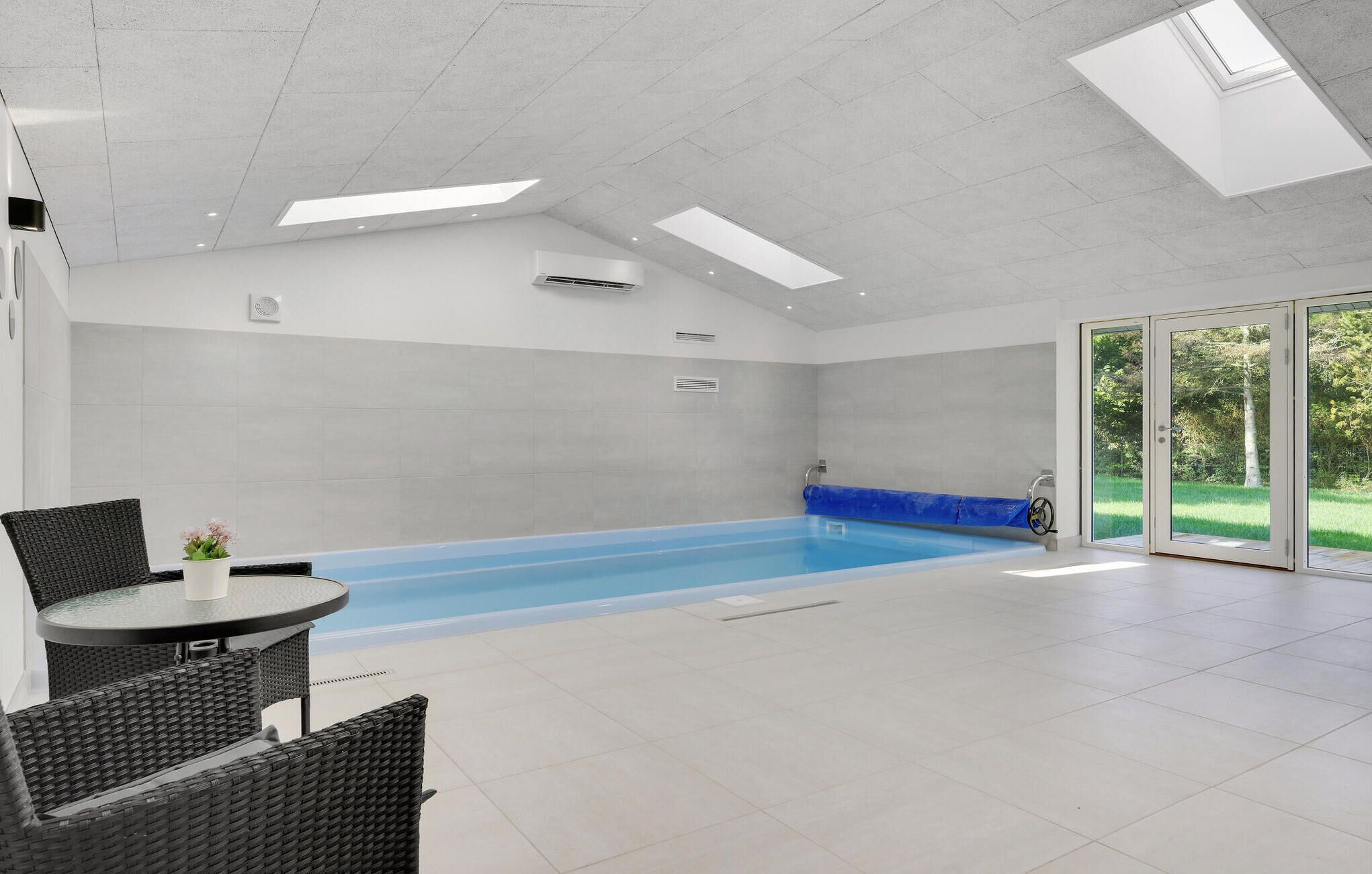 A modern indoor swimming pool with a glass door leading to a garden.