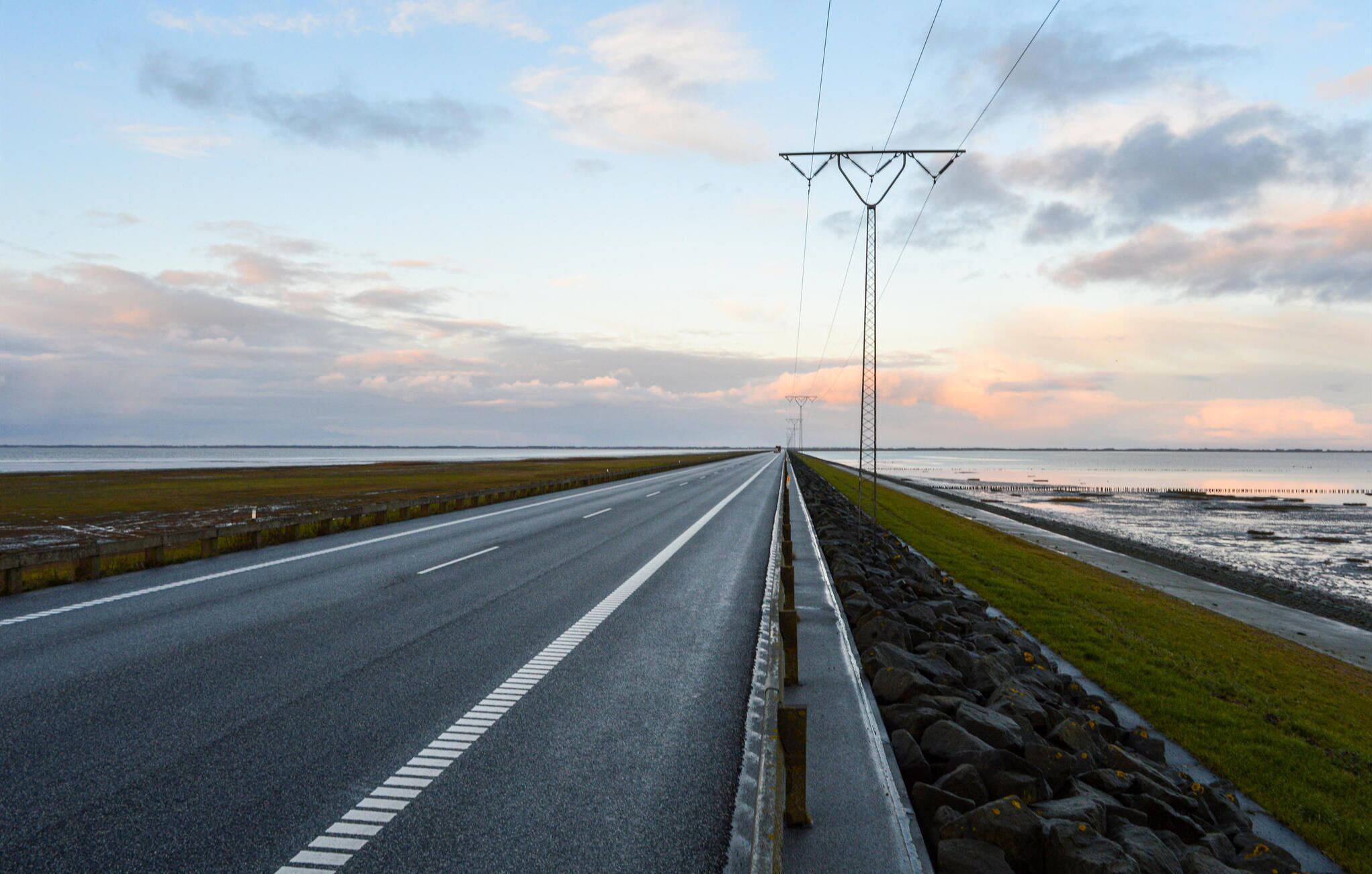 Une route côtière offrant une vue dégagée sur la mer et un coucher de soleil à l’horizon.