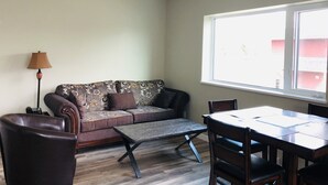 Een woonkamer met een bank, een salontafel, een eettafel met stoelen, een lamp en een raam met uitzicht op gebouwen.