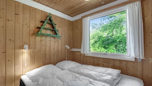 A bedroom with a wooden wall, a window with a view of greenery, a bed with white bedding, and a decorative wooden ladder. - Stunning home in Hasle with WiFi (Hasle)