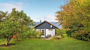 A small house with a dark roof and white walls, surrounded by lush greenery and trees with red fruits. - Stunning home in Hasle with WiFi (Hasle)