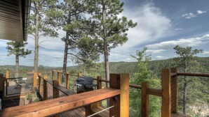 Eine Holzterrasse mit Grill und Sitzgelegenheit mit Blick auf eine bewaldete Landschaft.