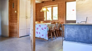 A wooden cabin interior with a dining table set for four, a window with a view of greenery, and a small refrigerator. - 3 bedroom cozy home in Jämshög (Jämshög)