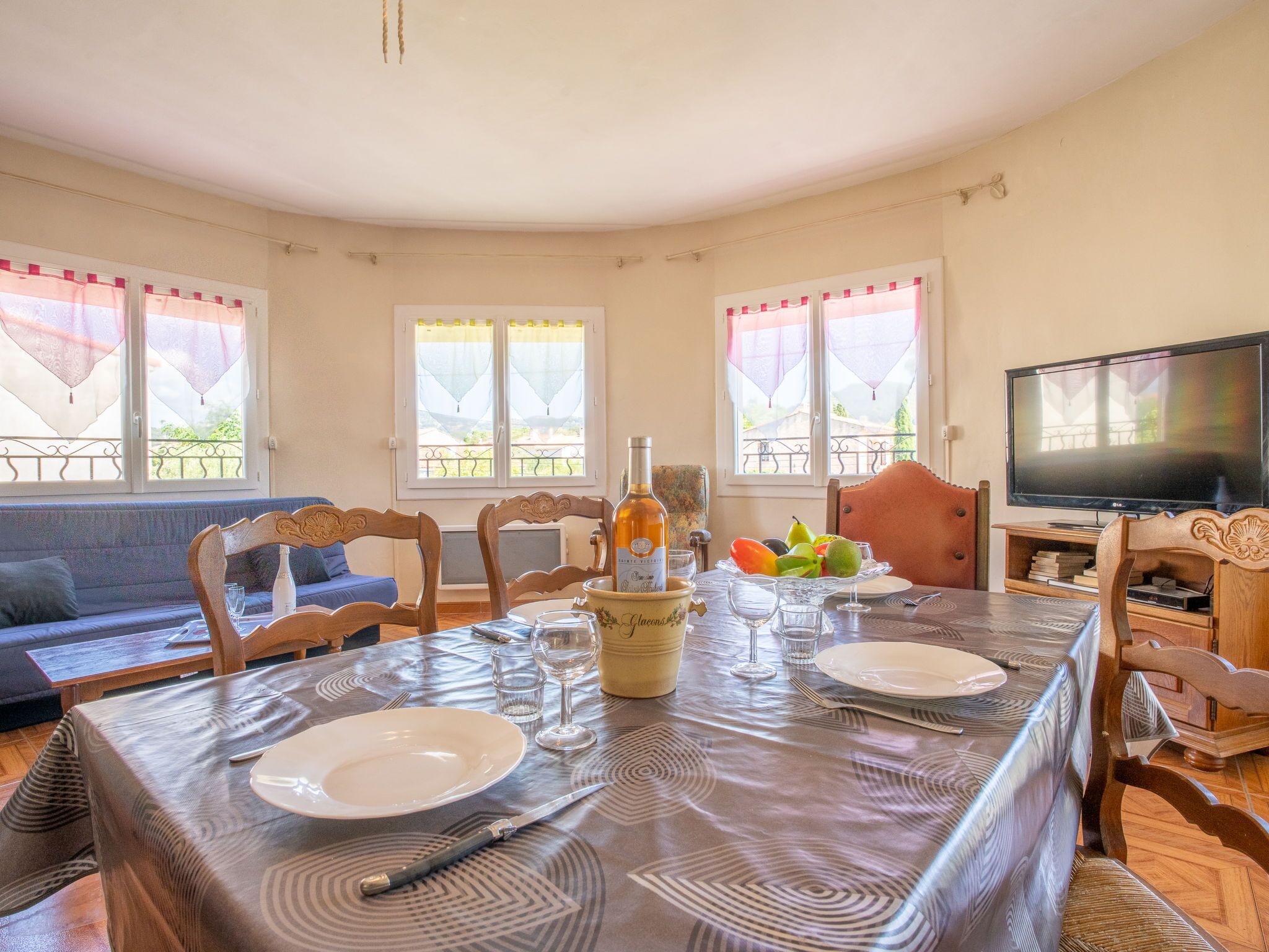 Un coin repas avec une table dressée pour deux personnes, une bouteille de vin et un panier de fruits.