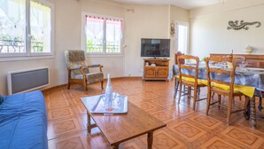 Ein Wohnzimmer mit einer Couch, einem Couchtisch, einem Fernseher und einem Essbereich mit Stühlen und einem für eine Mahlzeit gedeckten Tisch.
