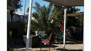 A covered outdoor seating area with a white roof, a bench, and a table. - KarMik Health & Wellness Retreat Cottage (Yuma)