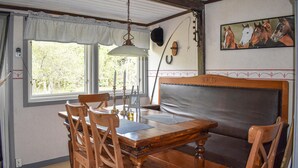 Un coin repas avec une table et des chaises en bois, un banc rembourré, un luminaire suspendu, un porte-manteau fixé au mur et un tableau représentant des chevaux.