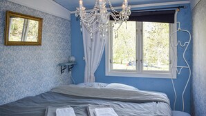 Une chambre à coucher avec un lit, un lustre, une fenêtre avec des rideaux, une petite table et un miroir.
