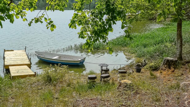 Un petit bateau était amarré à un quai en bois, avec une rive herbeuse et des arbres en arrière-plan.
