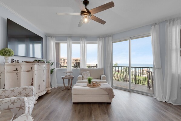 A spacious living room with a large window, a ceiling fan, and a view of the sea. - Any day at the beach is a good day! 🏖️ Book your vacay today! (Miramar Beach)