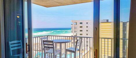 A balcony with a table and chairs, overlooking a beach and ocean.