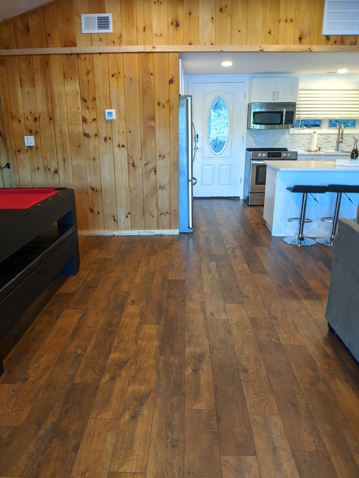 A room with wooden walls, a pool table, a kitchen with modern appliances, and a door leading to a balcony.