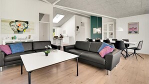 A modern living room with a black leather sofa, a white coffee table, and a dining area with a white table and black chairs.