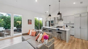 Una sala de estar moderna con un sofá gris, una mesa de centro de vidrio y una zona de cocina con armarios blancos y una isla central.