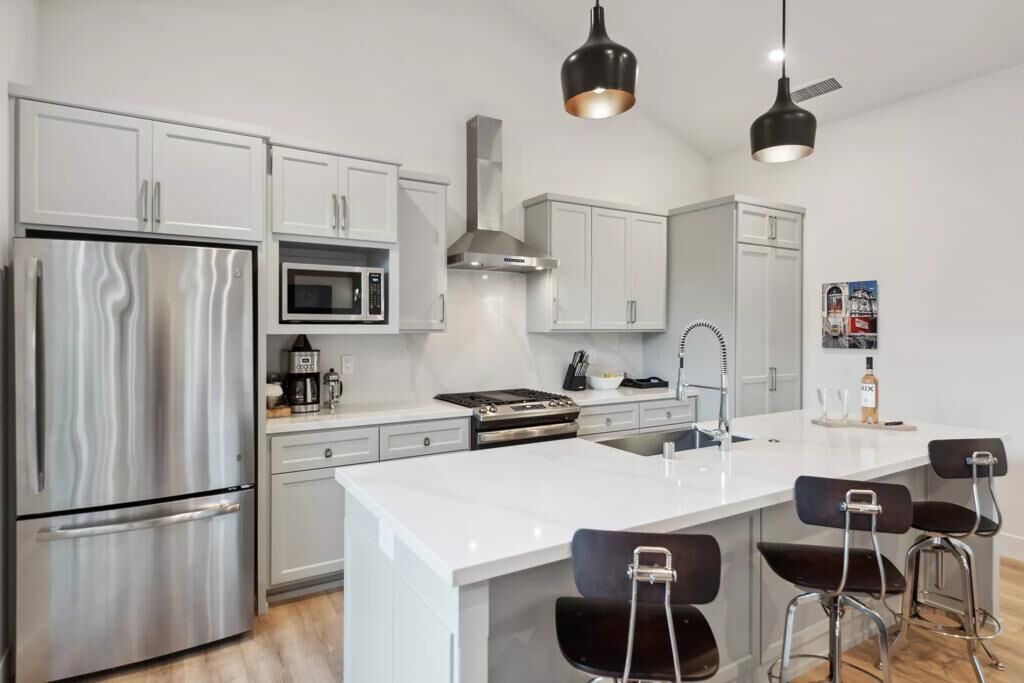 A modern kitchen with stainless steel appliances, white cabinetry, and a central island with bar stools.