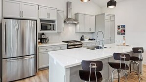 Una cocina moderna con electrodomésticos de acero inoxidable, armarios blancos y una isla central con taburetes de bar.