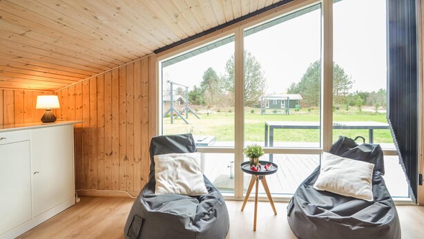 Ein Zimmer mit Holzwänden und einem großen Fenster. Zwei Sitzsäcke mit Kissen und ein kleiner Tisch mit einer Pflanze sind vorhanden.