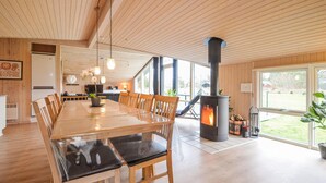Ein geräumiger Essbereich mit einem langen Holztisch und Stühlen, eine moderne Küche im Hintergrund und ein Kaminofen.