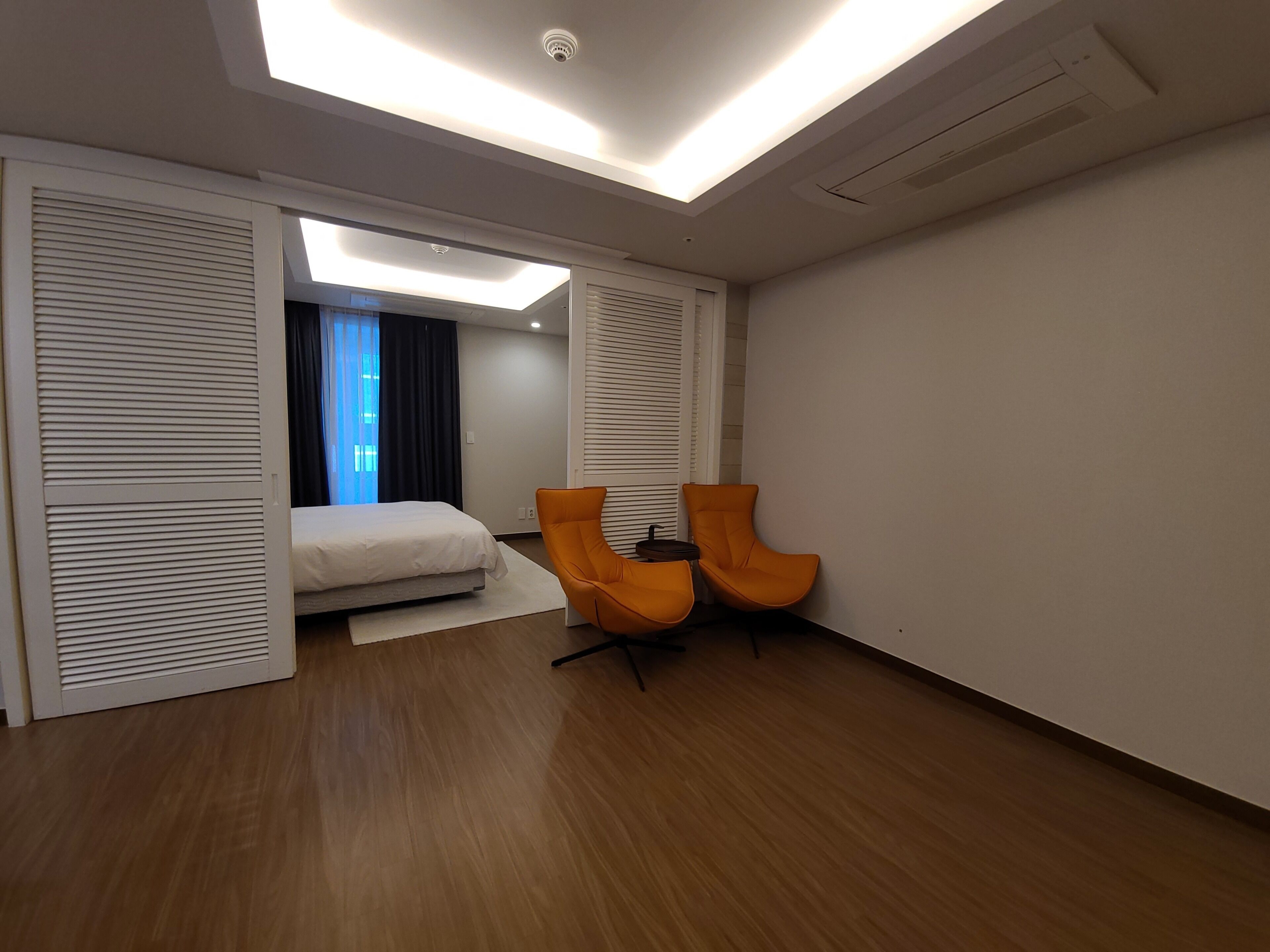 Ein modernes Hotelzimmer mit einem Bett, zwei orangefarbenen Sessel, einem Schreibtisch und einem Oberlicht.