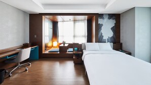 Une chambre d’hôtel moderne, dotée d’un bureau en bois, d’un canapé confortable, d’un lit et d’une grande fenêtre avec des rideaux.
