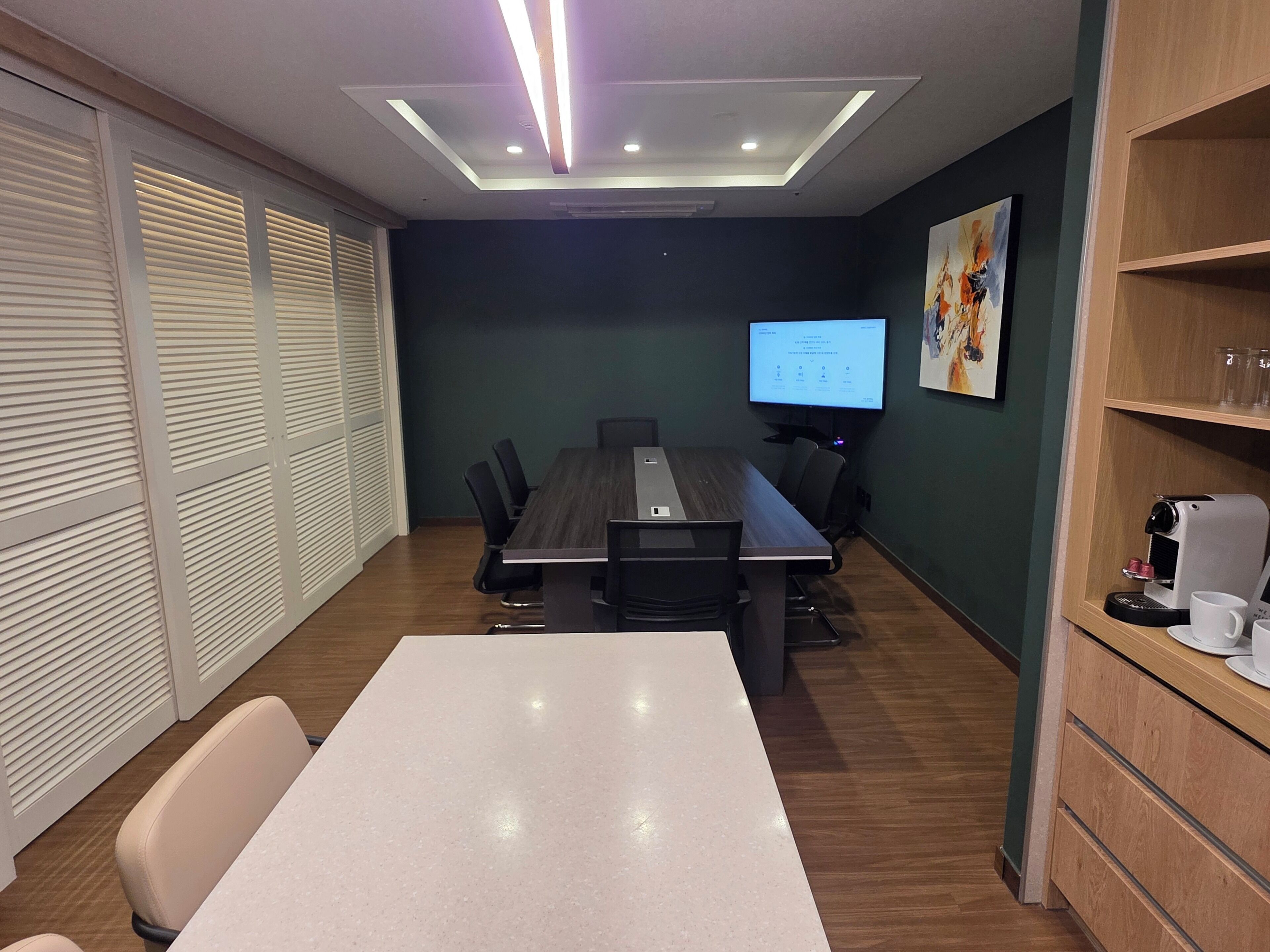 A conference room with a long table, chairs, a projector screen, and a coffee machine.