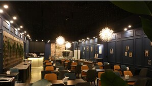 Un restaurant avec un long comptoir, plusieurs tables et des chaises. On y trouve des lampes suspendues et un mur en briques en arrière-plan.