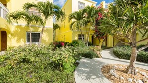 A yellow building with a garden, palm trees, and a pathway. - Just off the Beach, Relax at Inn At Grace Bay #121 (Grace Bay)