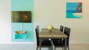 A dining area with a table, chairs, a TV, and a painting. - Just off the Beach, Relax at Inn At Grace Bay #121 (Grace Bay)