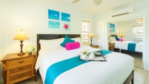 A hotel room with a bed, bedside lamps, a tray with breakfast items, and wall art. - Just off the Beach, Relax at Inn At Grace Bay #121 (Grace Bay)