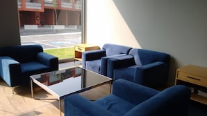 Uma sala de estar moderna com dois sofás azuis, uma mesa de centro de vidro e uma mesinha lateral de madeira.