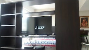 Quarto com televisão em um suporte, cama com colcha estampada e escrivaninha com um laptop.