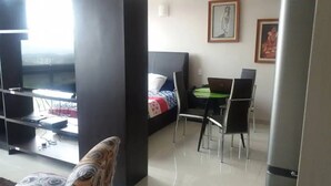 Quarto de hotel moderno com cama, escrivaninha, laptop, cadeira e televisão.