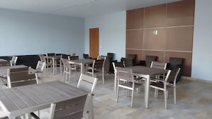 Sala de conferência com várias mesas e cadeiras, paredes azul-claras e uma porta de madeira.