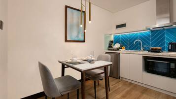 A modern kitchen with a dining area, featuring a wooden dining table, chairs, a pendant light, a blue backsplash, and stainless steel appliances.