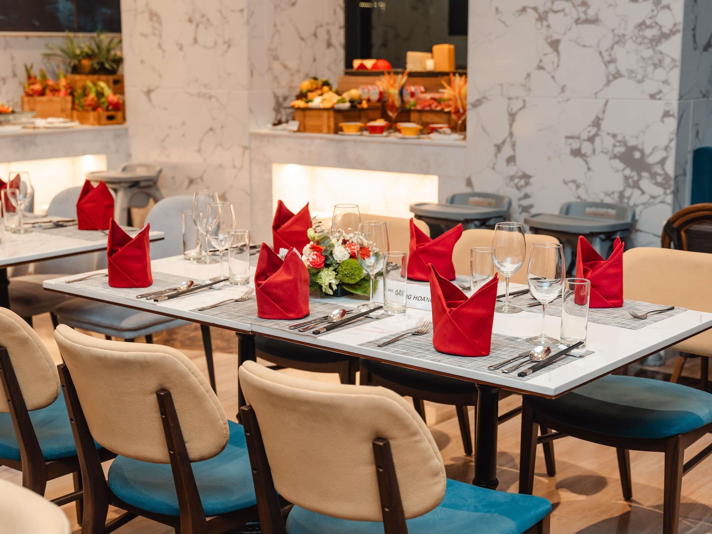 L’intérieur d ’un restaurant, avec des tables dressées pour le service, agrémentées de serviettes rouges et de verres transparents.