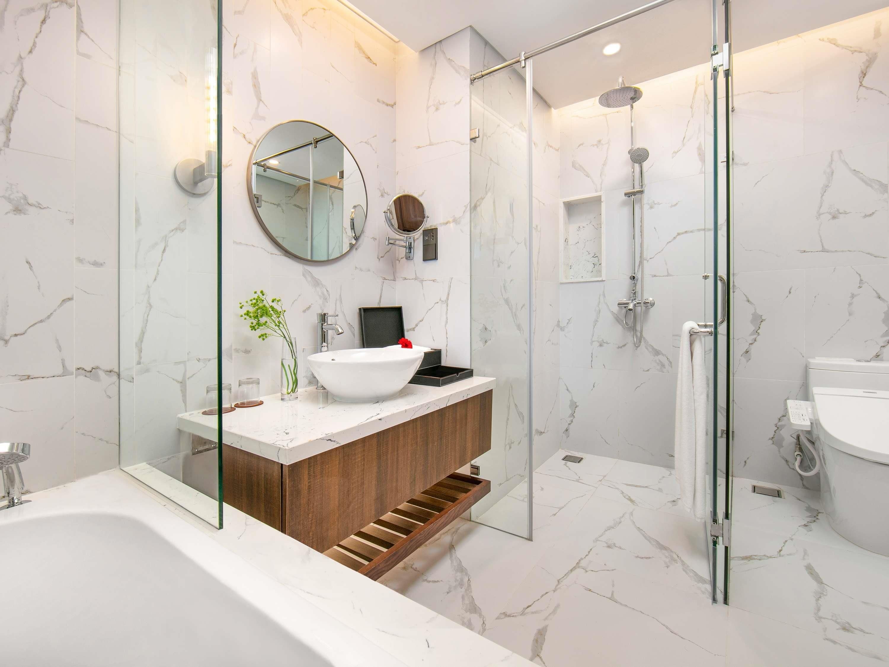 Une salle de bain moderne avec une douche à parois de verre, un lavabo blanc avec un meuble-vasque en bois et des murs en marbre.
