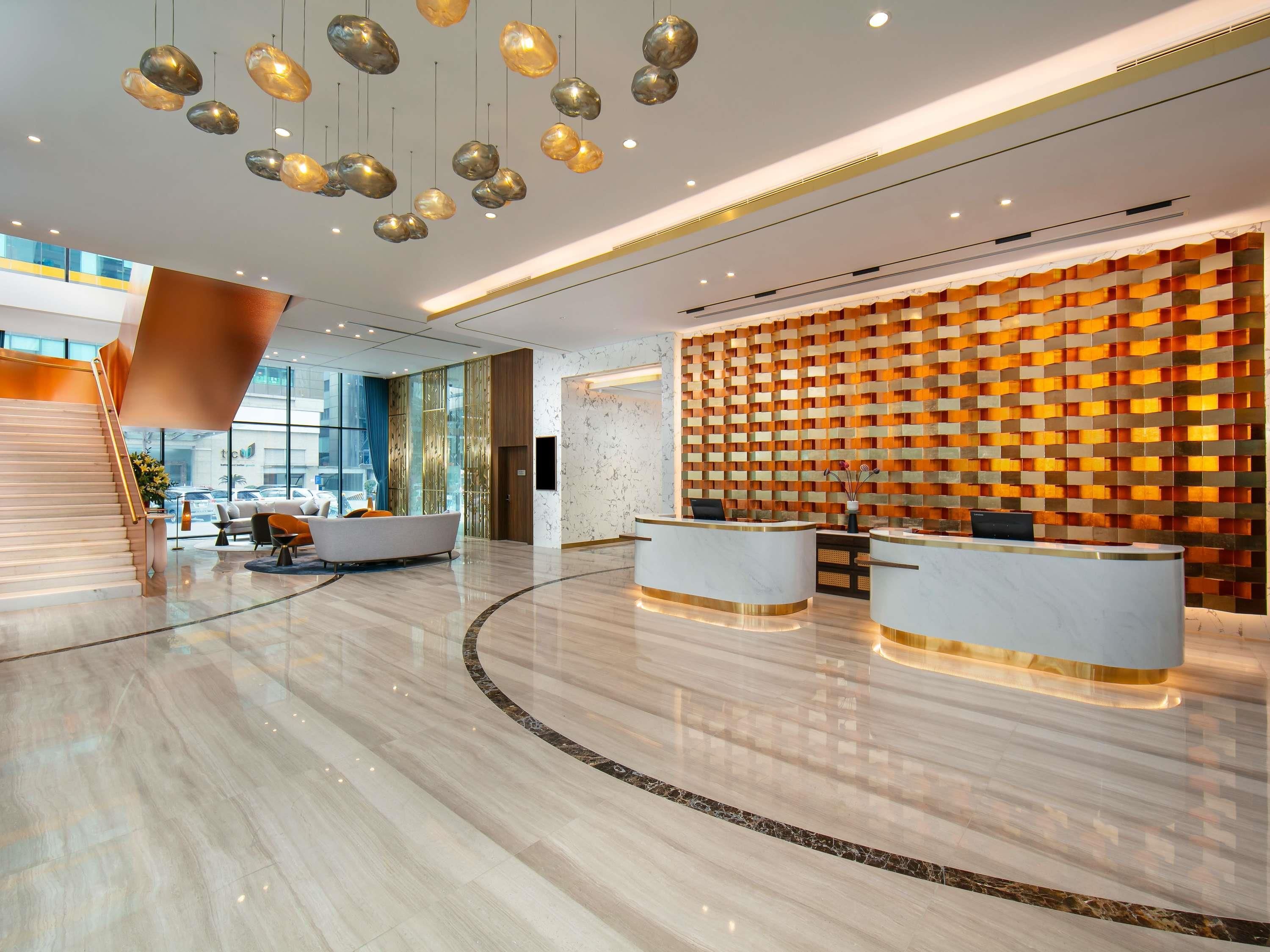 A modern hotel lobby with a reception desk, seating area, and a staircase.