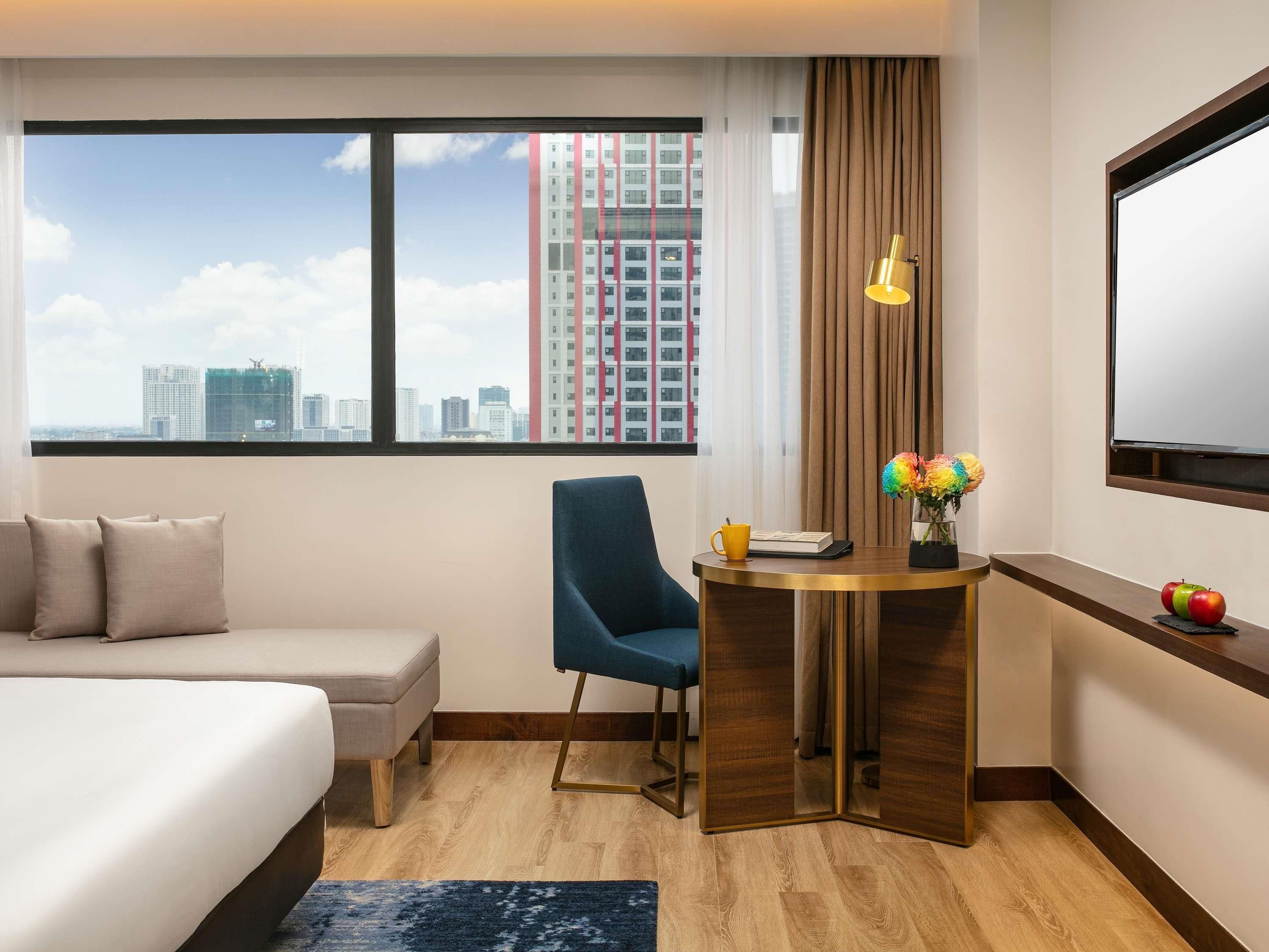 A hotel room with a bed, a desk, a chair, a window with a city view, and a TV.