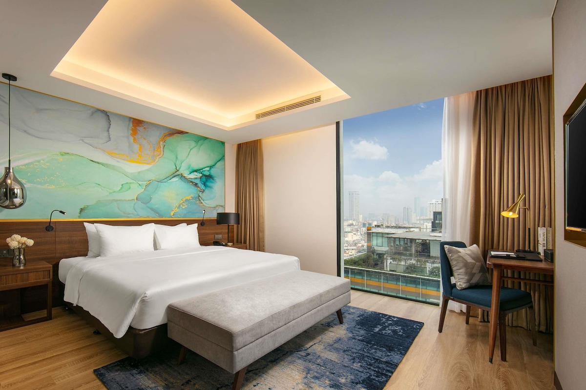 Een moderne hotelkamer met een groot bed, een bureau en uitzicht op de stad.