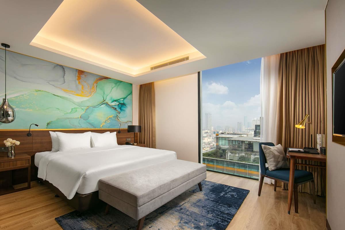Habitación de hotel moderna con una cama grande, un escritorio y vistas a la ciudad.