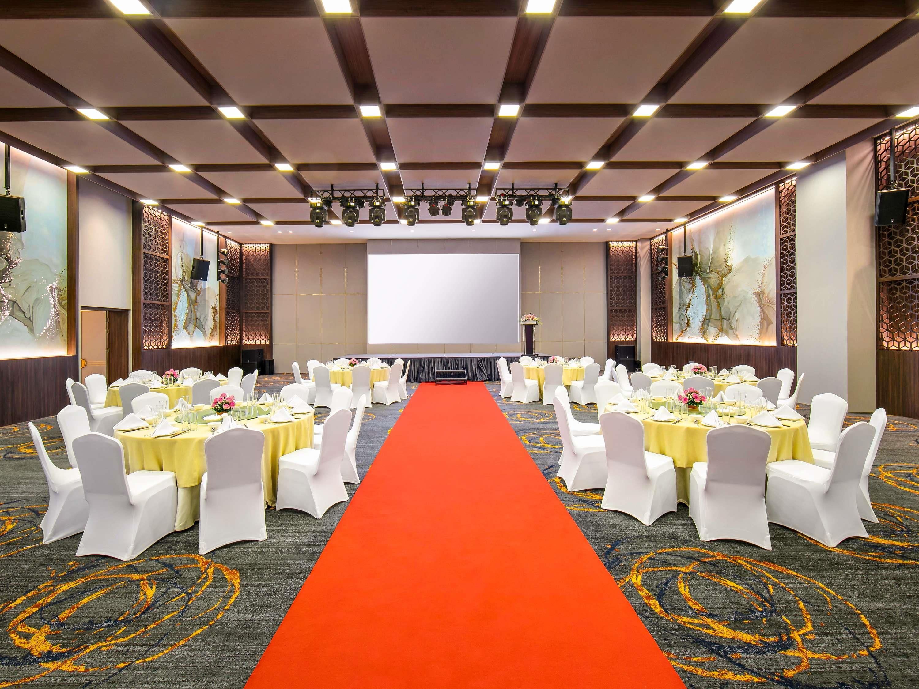 Un salón de conferencias con alfombra roja, sillas blancas y mesas dispuestas para una reunión.