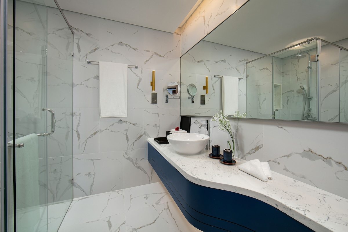 Une salle de bain moderne avec une douche à parois de verre, un lavabo en marbre blanc et un grand miroir.