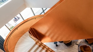 A modern interior with a curved staircase, marble flooring, and a seating area with round chairs.