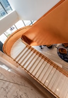 Un interior moderno con una escalera curva, suelo de mármol y una zona de estar con sillas redondas.
