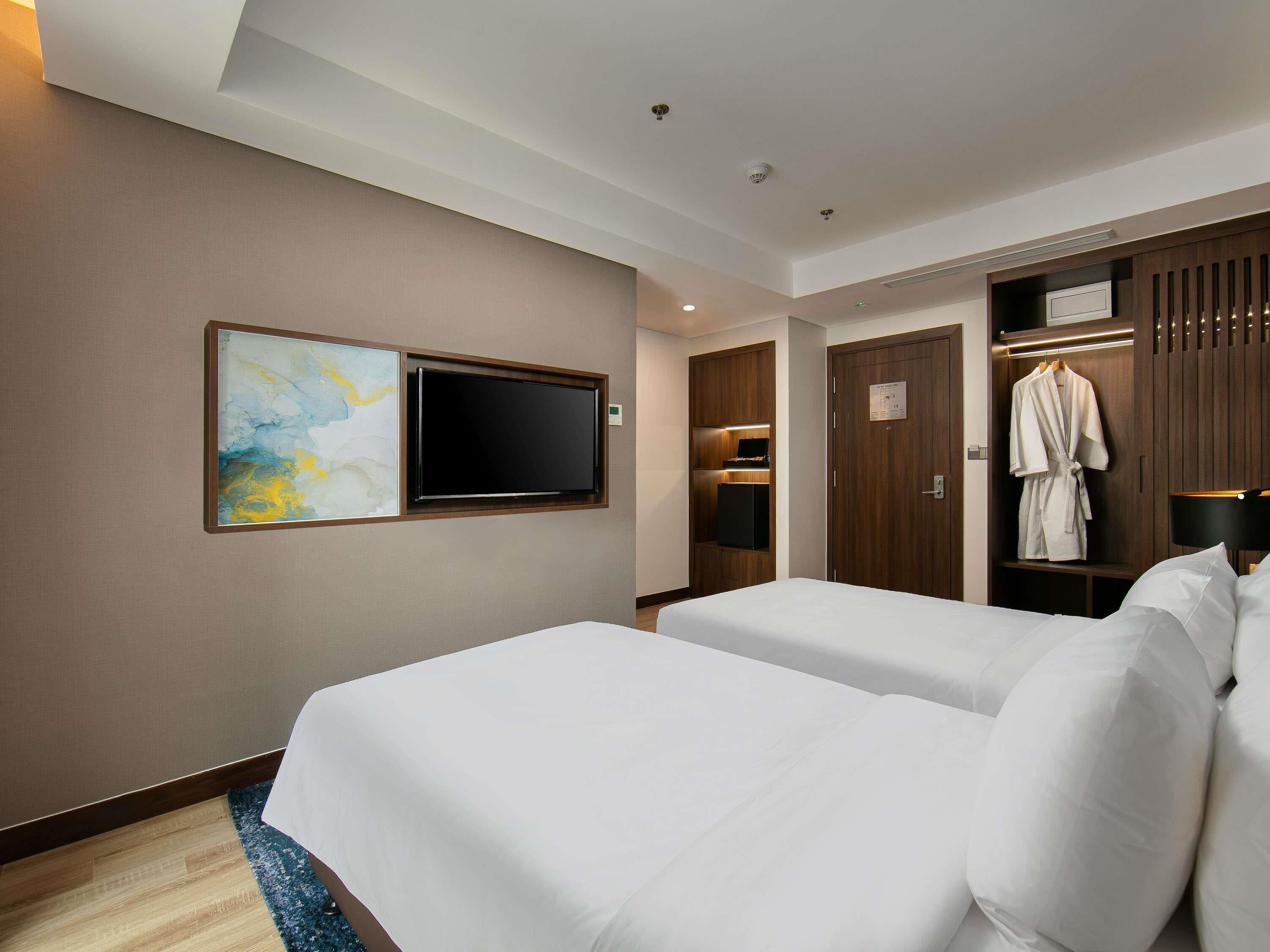 Habitación de hotel con dos camas, un televisor de pantalla plana, una bata colgada en la puerta y un cuadro en la pared.